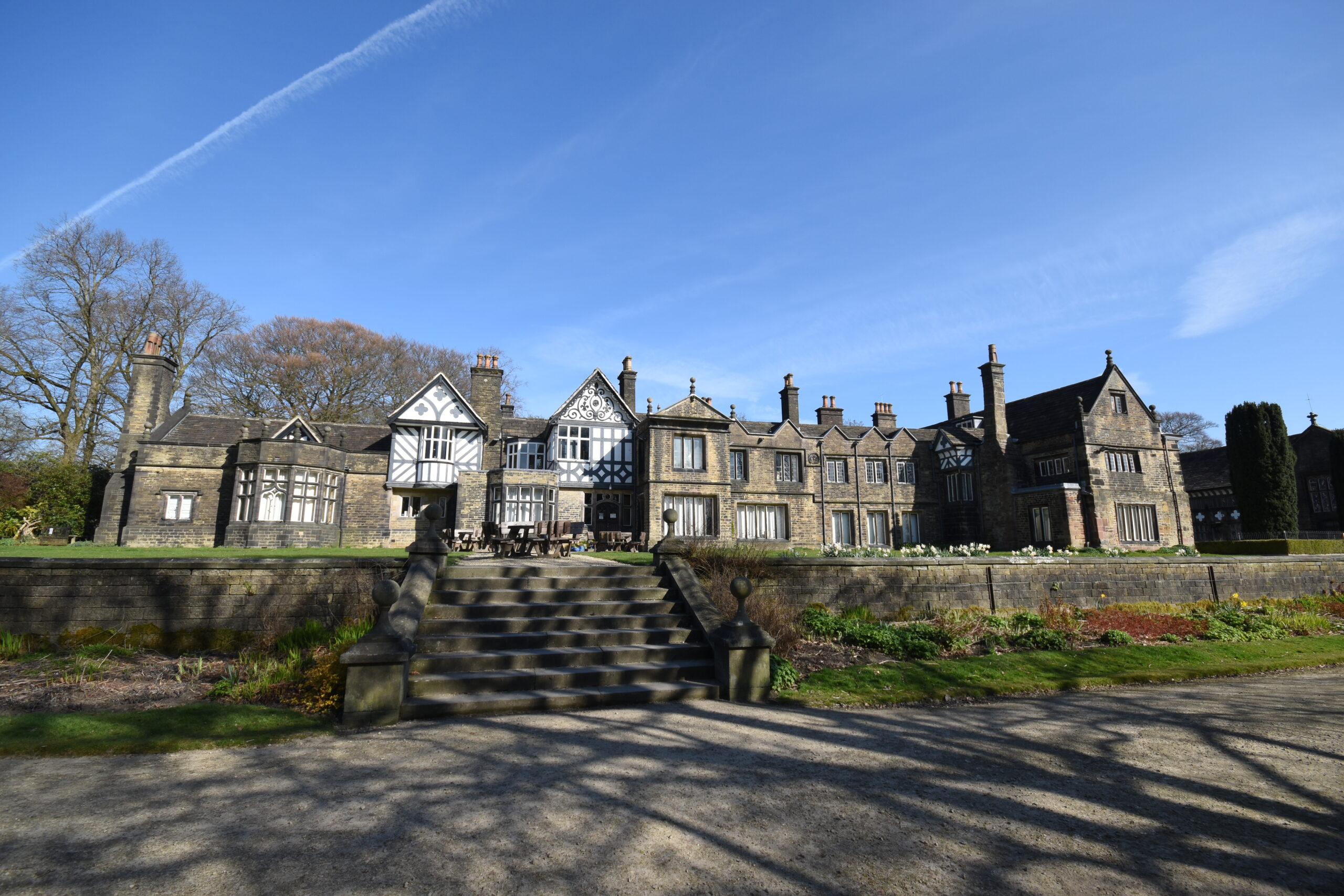 Smithills Hall exterior showcasing Tudor style architecture. A maintained lawn out the front with wooden seating.